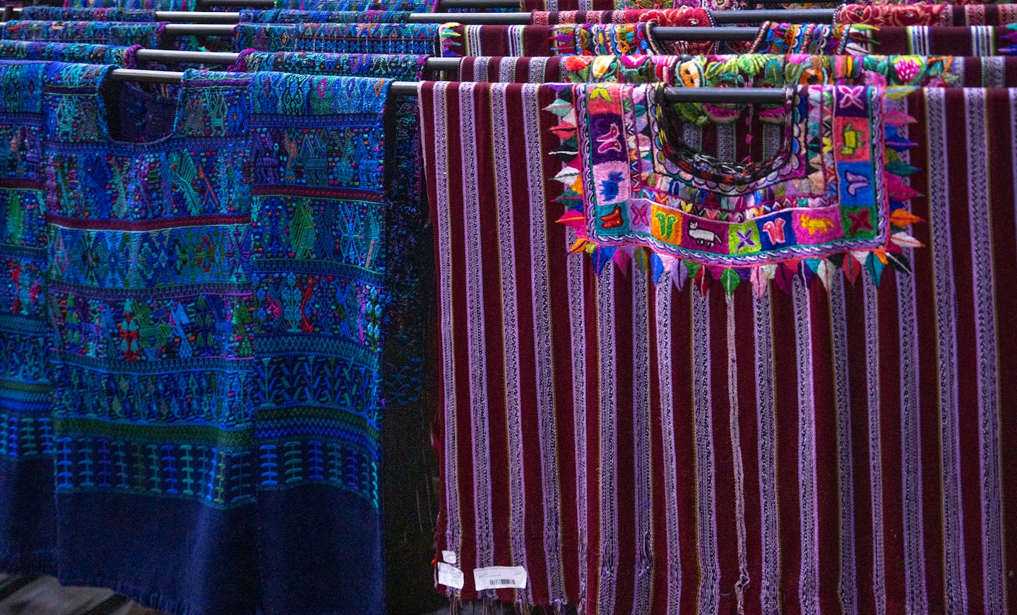 Textiles bordados tradicionales cuelgan en expositores metálicos.