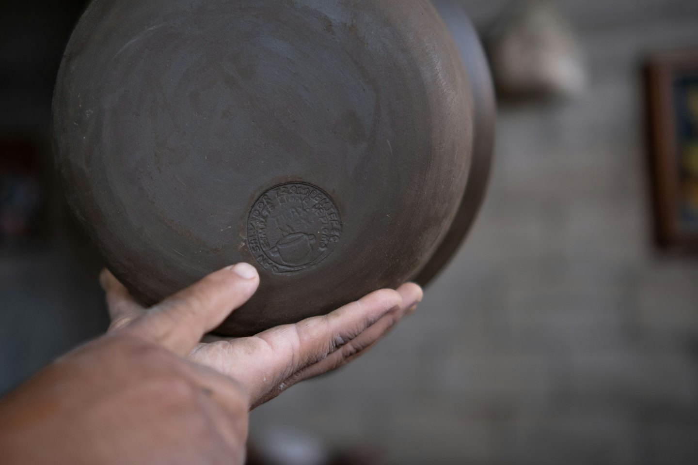 Mano sosteniendo una maceta de cerámica sin esmaltar con un logo.