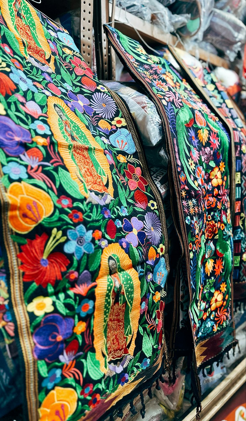 Textiles intrincadamente bordados con motivos florales y figuras religiosas colgados en una tienda.